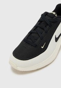 Crna i krem tenisica za sport s teksturiranim mrežastim gornjim dijelom, ravnim vezicama i istaknutim swoosh logom sa strane.