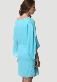 Vestido azul claro de corte holgado, con mangas murciélago y un detalle tejido en el escote. Presenta una cintura anudada y una textura suave.