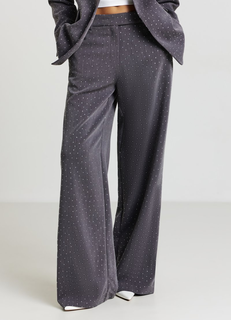 Pantaloni grigi a gamba larga in tessuto morbido con un motivo a puntini bianchi di piccole dimensioni. Presentano una cintura piatta e un design sobrio con linee pulite.