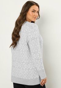 Jasnoszary sweter z delikatnym wzorem geometrycznym, prążkowanymi mankietami i dołem oraz luźnym krojem, pokazany z boku.
