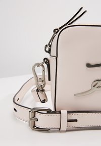 Kompaktowa różowa skórzana torebka crossbody z srebrnymi akcentami, górnym zamkiem błyskawicznym i regulowanym paskiem z kontrastowym przeszyciem oraz detalem logo.