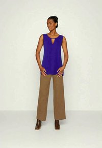 Top roxo sem mangas com decote em buraco de chave, combinado com calças largas em bege e botas de tornozelo castanhas. Textura mate em toda a peça.