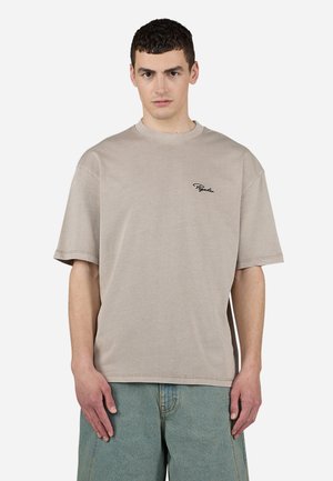 Beige oversized t-shirt with short sleeves, ribbed crew neckline, and embroidered logo on the left chest, paired with light denim shorts.