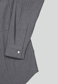 Gray button-up shirt with a textured pattern, featuring a single-button cuff and a curved hem design. Tag visible on the side.