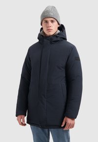 Marineblauwe geïsoleerde parka jas met capuchon, voorzien van een rits- en drukknoopsluiting, zijzakken en een gestructureerde grijze gebreide muts.