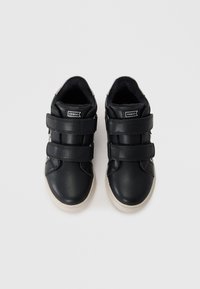 Svarte lær sneakers med to borrelåsremmer, rund tå og kontrasterende hvit gummisåle. Har en subtil logo på siden.