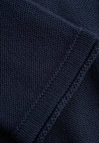 Tamsiai mėlynas megztas audinio fragmentas su tekstūruotu pynimu; turi briauna su arbaelėmis ir lygų siuvimą šone.