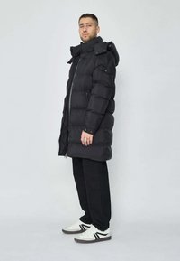 Doudoune noire avec un col haut, fermeture éclair à l'avant et poches latérales. Associée à un pantalon noir et des baskets blanches avec des accents noirs.