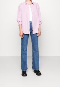 Vaaleanpunainen raidoitettu nappipaita, jonka hihat on kääritty, yhdistetty sinisiin farkkujen leveisiin lahkeisiin ja mustiin nilkkureihin. Yksinkertainen muotoilu ja rento istuvuus.