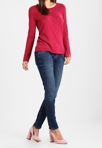 Maglietta fucsia a maniche lunghe, jeans skinny blu scuro e scarpe rosa con tacco spesso. Tessuto morbido, design aderente, aspetto casual ma curato.