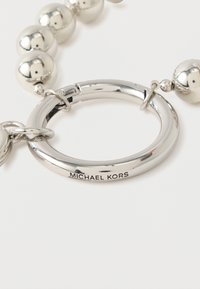 Hopeanvärinen metallinen avaimenperä, jossa pyöreitä helmiä, suuri pyöreä rengas ja kaiverrettu "MICHAEL KORS" -logo brändin tunnistamiseksi.