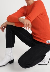 Ribbade orange tröja med långa ärmar, matchad med mörka jeans och vita ankelskor. Anmärkningsvärd märkesdetalj vid tröjans nederkant.