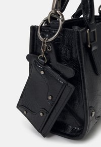 Sac à main en cuir noir texturé avec une petite pochette assortie fixée par un anneau métallique et une chaîne sur un fond blanc.