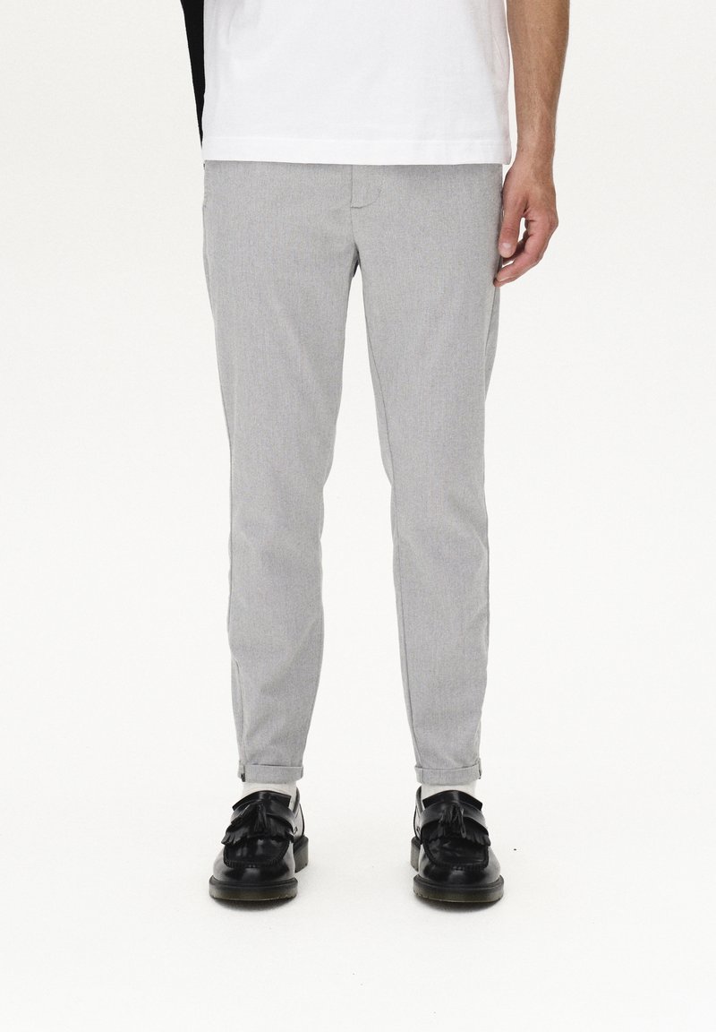 Grå, slim-fit byxor i texturerat tyg, med flat front och framfickor. Bärs med svarta skor med detaljer i form av fransar.