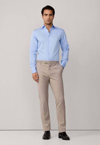 Lichtblauw overhemd met knopen en een slanke pasvorm, beige op maat gemaakte broek en zwarte schoenen. Glad stoffen textuur en subtiele ontwerpelementen.