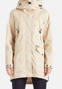 Jasnobeżowa, wodoodporna parka z kapturem, zamkiem z przodu, dużymi kieszeniami i regulowanymi sznurkami. Gładka tekstura i długość do połowy uda.