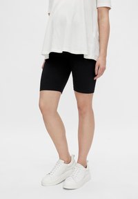 Un short de vélo noir en tissu extensible, associé à un t-shirt blanc ample et à des baskets blanches, mettant en avant une tenue décontractée.