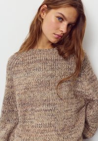 Neulepusero, jossa beige ja taupen sävyjen yhdistelmä, rento istuvuus, pyöreä pääntie ja erilaisilla paksuuksilla varustettu kuvio.