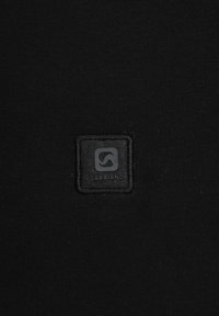 Tessuto nero con un patch quadrato nero con il testo in rilievo "GABBIANO" e un design del logo curvo, il tutto su uno sfondo testurizzato.
