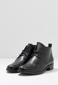 Bottes noires à la cheville en matériau synthétique texturé, avec un bout arrondi, un talon plat et un design de lacets contrastants.