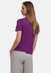 Paarse korte mouwen T-shirt van zacht materiaal, met een eenvoudige ronde halslijn en een relaxte pasvorm, gecombineerd met grijze broek.