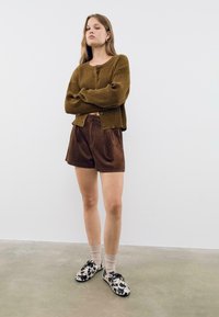 Cardigan côtelé marron avec boutons à l'avant, associé à un short en velours marron. Chaussures à motifs noir et blanc avec des chaussettes claires.