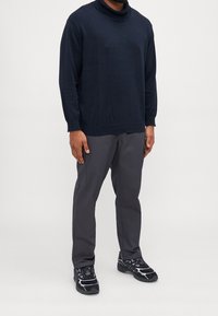 Pull col roulé bleu marine, matière douce, coupe décontractée. Pantalon gris avec poches, coupe fuselée. Baskets noires avec accents réfléchissants et violet.