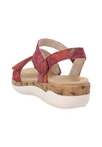 Sandale rouge avec des sangles texturées et une fermeture velcro ajustable. Semelle en liège avec une semelle en caoutchouc blanche. Design plat, dos ouvert.