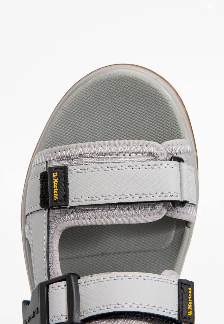 Nahaufnahme einer grauen Dr. Martens Sandale mit verstellbaren Klettverschlüssen und strukturiertem Fußbett auf einem weißen Hintergrund.