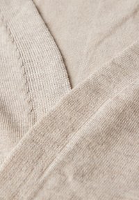 Beige tyg med en mjuk textur och räfflade kanter, med en lagerdesign och subtila variationer i vävningsmönster.