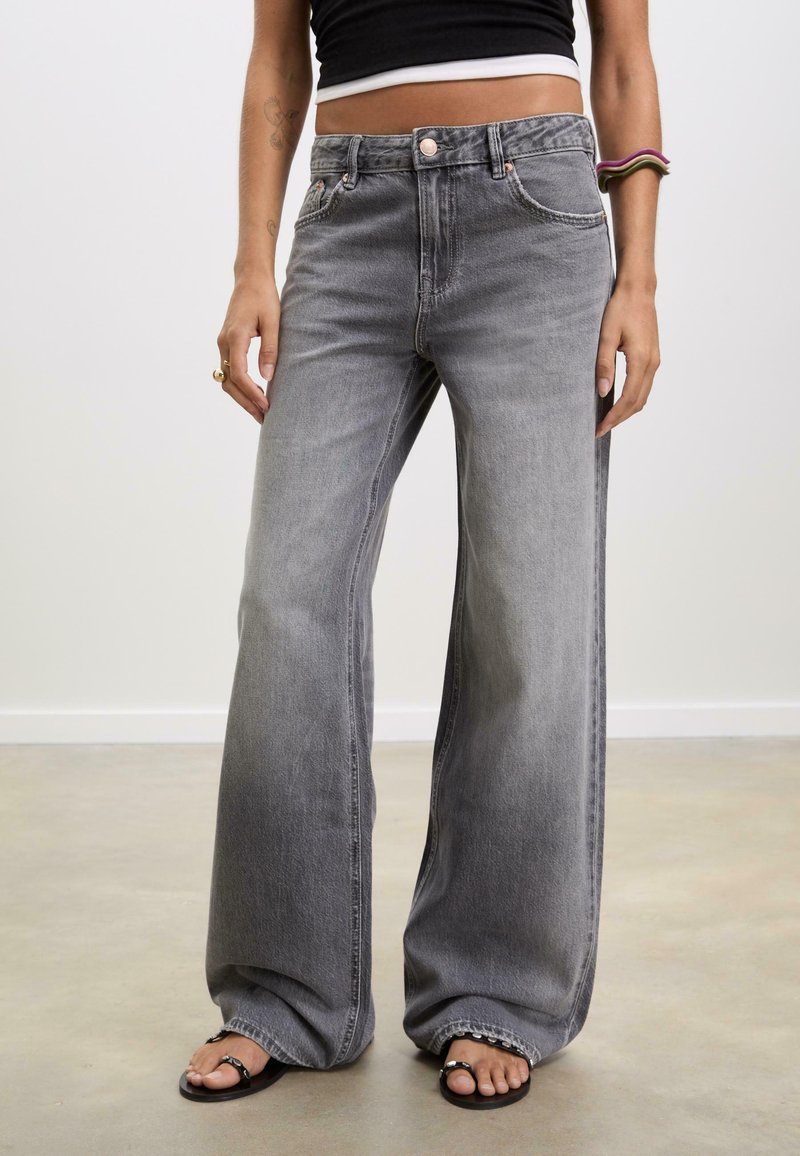Jeans in denim grigio a gamba larga con vita alta, cuciture visibili e una leggera sfumatura. Presentano tasche frontali e chiusura con bottone.