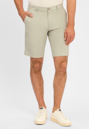 Shorts en coton vert clair avec une coupe droite, des poches latérales et une fermeture à bouton. Associés à des baskets beiges pour un look décontracté.