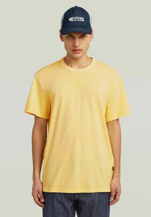 T-shirt di cotone gialla con maniche corte e colletto a girocollo, abbinata a un cappellino da baseball blu navy con logo bianco e retro in rete.