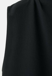 Zachte zwarte stof met zichtbare stiksels langs de rand, gedrapeerd tegen een lichte achtergrond die textuur- en vouwdetails toont.