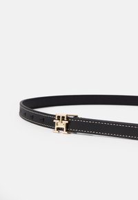 Črn usnjen pas z zlatimi dodatki, ki ima sponko z medsebojnim dizajnom in kontrastno belo šivanje ob robovih.