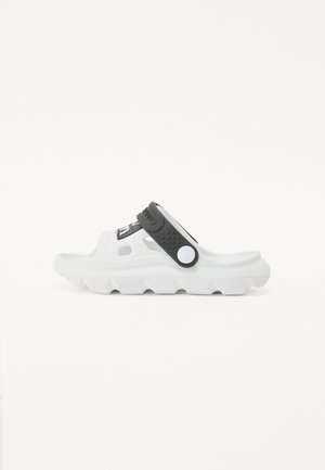 Sandal desportivo branco com sola espessa, tira preta ajustável e detalhes texturizados. Apresenta orifícios de ventilação e um logótipo proeminente.