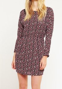 Blommig klänning med långa ärmar, med en mörk vinröd bakgrund och små vita och rosa blommor. Lätt tyg, åtsittande midja, kort längd.