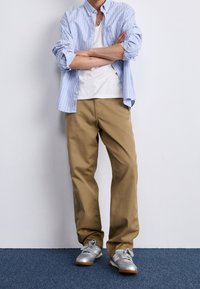 Light blue and white striped long-sleeve shirt over a white t-shirt, paired with tan pants and silver athletic shoes.