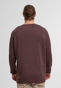 Bordeauxroter Strickpullover mit geripptem Kragen und Bündchen, mit lockerer Passform und längerem Rückensaum, aus weichem Stoff für besonderen Komfort.