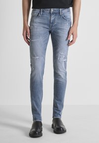 Svijetlo plave slim-fit traperice izrađene od denima, s prorezima i suženim nogavicama. Uparene s crnim čizmama do gležnja.