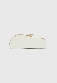 Bela podlaga sandala z teksturirano gumijasto podplatom, pluto podlogo in zlatim zaponko. Dizajn je raven in z odprtimi prsti.