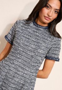 Rövid ujjú ruha texturált tengerészkék és fehér anyagból. Kerek nyakú, töredezett tengerészkék szegéllyel, és testhezálló szabással.