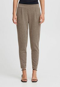 Bruine broeken met een visgraatmotief, tapered fit en een elastische tailleband. Gecombineerd met zwarte, gespen sandalen.