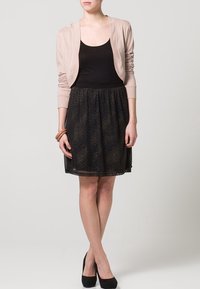 Svart tyllkjol med gyllene prickar, matchad med en figurnära svart linne och en ljusrosa cardigan. Outfiten inkluderar svarta klackar.