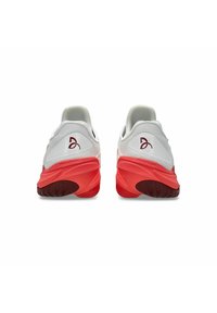 Hvide sportsko med en tekstureret mesh-overdel og en rød gummisål, der har en lavere hæl og logodetalje på hælen.