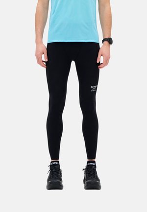 Mann trägt schwarze Kompressionsleggings, schwarze Laufschuhe, schwarze CEP-Socken, hellblaues Sportshirt und eine schwarze Armbanduhr.