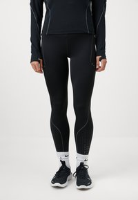 Zwarte sportleggings met contrasterende stiksels, ademende stippenaccenten en een soepele textuur, gecombineerd met zwarte sportschoenen en witte sokken.