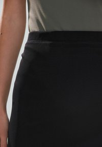 Čierna, priliehavá sukňa s hladkou textúrou a elastickým pásom. V kombinácii s svetlo olivovo zeleným vrchom, ktorý zdôrazňuje štíhlu siluetu.