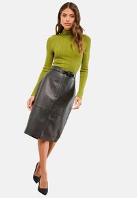 Žalias ralio rašto megztinis su stovu ir juoda odinė pieštuko sijonas su diržu talijoje. Juodi aukštakulniai batai užbaigia aprangą.