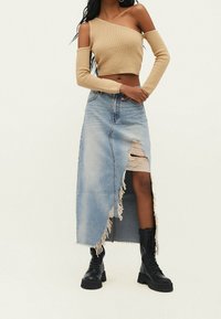 Beige ribfluwelen off-shoulder top gecombineerd met een lichtblauwe distressed denim maxi rok met een gescheurde zoom en een zijslit, gedragen met zwarte laarzen.